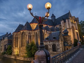 Gothic cathedral at dusk with illuminated streetlamp in the foreground, situated at the water