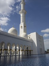 The magnificent mosque with domes and minaret is reflected in the clear water of the pool under a