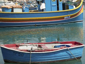 A small red boat and a larger fishing boat moored in the harbour, many colourful fishing boats in a