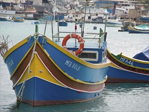 Front view of a colourful boat and another boat next to it in a quiet harbour, life ring visible,