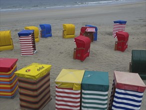 Colourful beach chairs spread out on the beach in different colours under a cloudy sky, beach