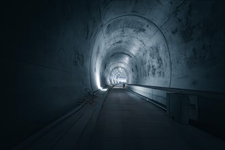 An empty tunnel with concrete walls and light sources on the sides, which has a dark, mysterious