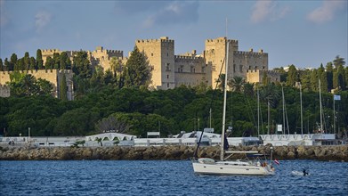 Historic castle by the sea with yacht in the foreground and cloudy sky, trees, Grand Master's