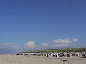 Wide beach with blue sky and clouds, rows of beach chairs and dunes, dunes and beach at the sea