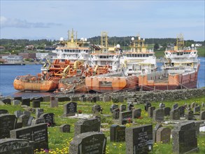 Cemetery with gravestones and several ships in the background under a slightly cloudy sky, old