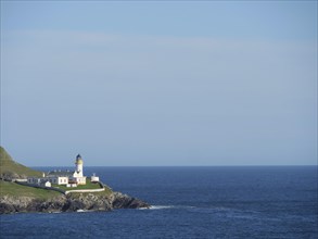 Lighthouse on the coast, surrounded by grassland and blue sea under a clear sky, white lighthouse,