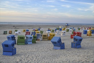 Colourful beach chairs on a wide sandy beach at dusk with a view of the sea, many colourful beach