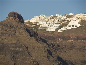White buildings on a steep slope with rocks in the foreground under a clear blue sky, rocky island