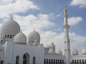 White mosque with several domes and a high minaret under a cloudy sky, large mosque with white