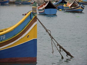 A yellow-blue boat is moored to the harbour with a rope, surrounded by other boats, many colourful