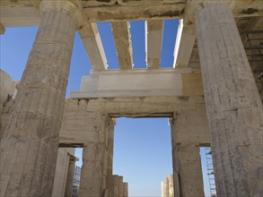 A temple window with a view of ancient columns and blue sky, historic columns and ruins at an