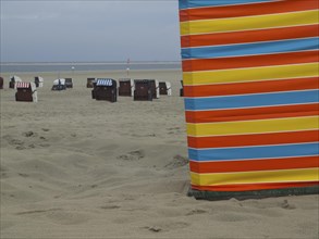 A colourful strip of sand on the beach with beach chairs in the background, extensive sand, beach