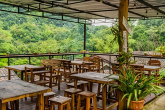 Empty tables and chairs on covered balcony of restaurant overlooking rainforest in Thailand