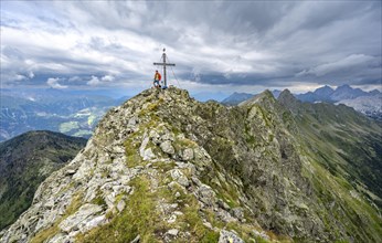 Mountaineer on the rocky pointed summit of the Raudenspitze or Monte Fleons with summit cross,