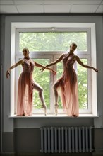 Silhouette of two ballerinas perform dance moves while standing on a windowsill in a hallway