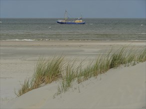 Blue boat in calm sea behind sand dunes with reeds, dunes by the sea with clouds in blue sky, nes,