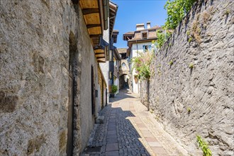 Narrow alley with cobblestone alleyway and old buildings, surrounded by stone walls and flowers,