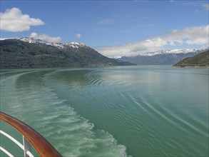 Boat trip on a clear water surrounded by snow-capped mountains and blue sky, greenish shimmering