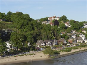 Coastal view with houses along the beach and lush greenery on the hills under a clear sky, green