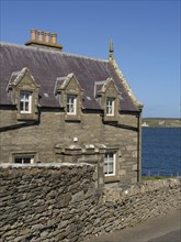 Stone building with skylights behind a stone wall, on a clear day by the sea, old stone house by
