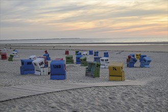 Atmospheric evening sun on a quiet beach with colourful beach chairs and a wooden walkway in the