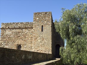 Old building on a stone wall, behind it a tree and a clear blue sky, stone walls of an old Moorish