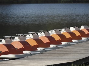 Several orange and white pedal boats are neatly moored in rows on the jetty, rowing boats and pedal