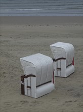 Two white beach chairs stand abandoned on a quiet beach in front of a cloudy sky, beach chairs and