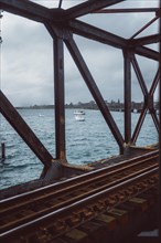 Rusty railway bridge with lake and boats in the background. Cloudy day over Tauranga, New Zealand,