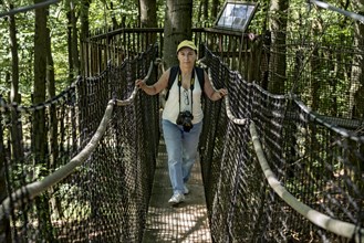 Sporty woman, tourist with camera in treetop path, suspension bridges, ropes, nets, beech forest,