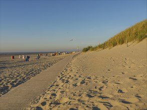 A long sandy path along high dunes to the sea in sunny weather and quiet atmosphere, sunset on a