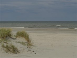 A quiet beach with dune grass and a cloudy sky, dune with dune grass and a boat by the sea, clouds