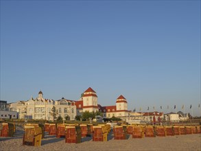 Beach chairs on the beach in front of a large building with red towers and waving flags under a