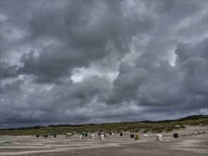 Stormy beach with clouds and scattered beach chairs, surrounding dunes, colourful beach chairs on