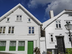 Historic white wooden houses with green doors and windows under a blue sky, illuminated during the