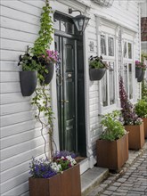 A charming white house with flower arrangements and a black door, white wooden houses with green