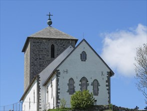 White church with stone tower, close-up under blue sky with clouds, old stone church and many