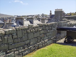 A cannon stands behind a stone wall overlooking the town, old cannons on a stone wall by the sea