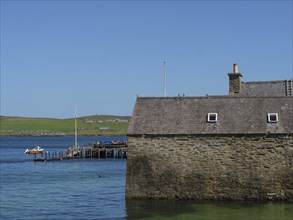 Old stone building on the water with a small jetty and a boat in the clear blue sea, old stone