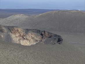 Volcanic crater in a grey desert landscape with a view of the ocean and blue sky, barren landscape