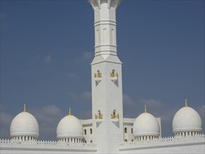 Minaret of the mosque with white domes and golden details under a blue sky, beautiful mosque with