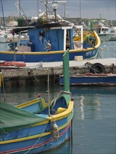 Small colourful boats moored in the water with other boats and huts in the background, many