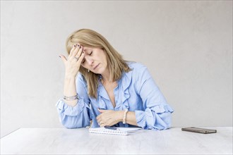 A mid-adult blonde woman is holding one hand on her forehead