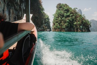 Boat surrounded by emerald green water and wooded cliffs. Khao Sok National Park, Thailand, Asia