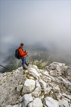 Mountaineer on a rocky narrow summit ridge, cloudy mountain peak, summit of the Great Kinigat,