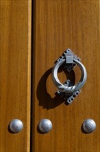 Latch on a wooden door with metal rivets illuminated by sunlight with shadows