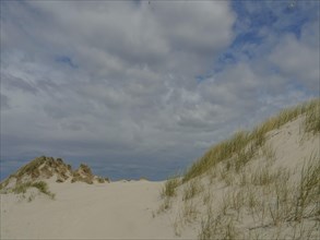 Landscape with sand dunes and grass under a partly cloudy sky, quiet and secluded, dunes on an