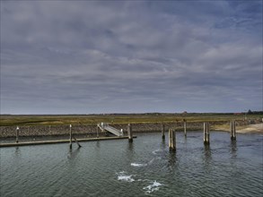 A long jetty in the sea with a cloudy sky and coastal landscape in the background, small jetty with