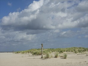 Beach landscape with sand dunes and blue sky, covered with clouds, peaceful atmosphere, lonely