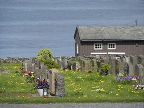 Colourful cemetery with flowers in front of a wooden house on the shore of a lake, old stone church